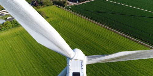 Aerial close up photo of wind turbine providing sustainable energy by spinning blades the power also known as renewable is collected from resources green field meadow in background
